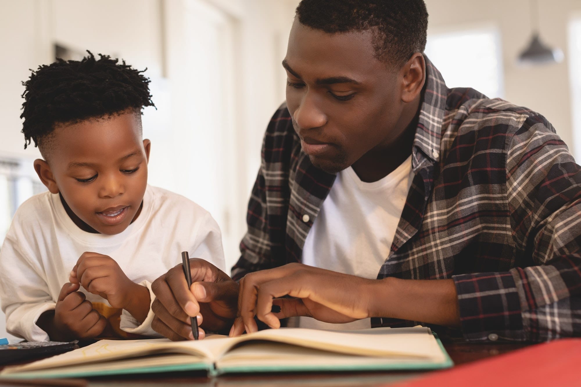 Front view of African American father helping his son with homework at table