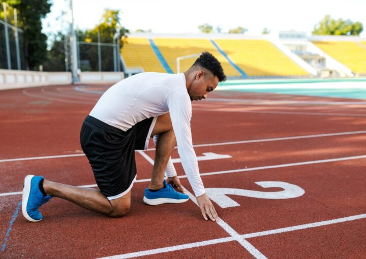 Young attractive African American sportsman preparing for running on racetrack at city stadium