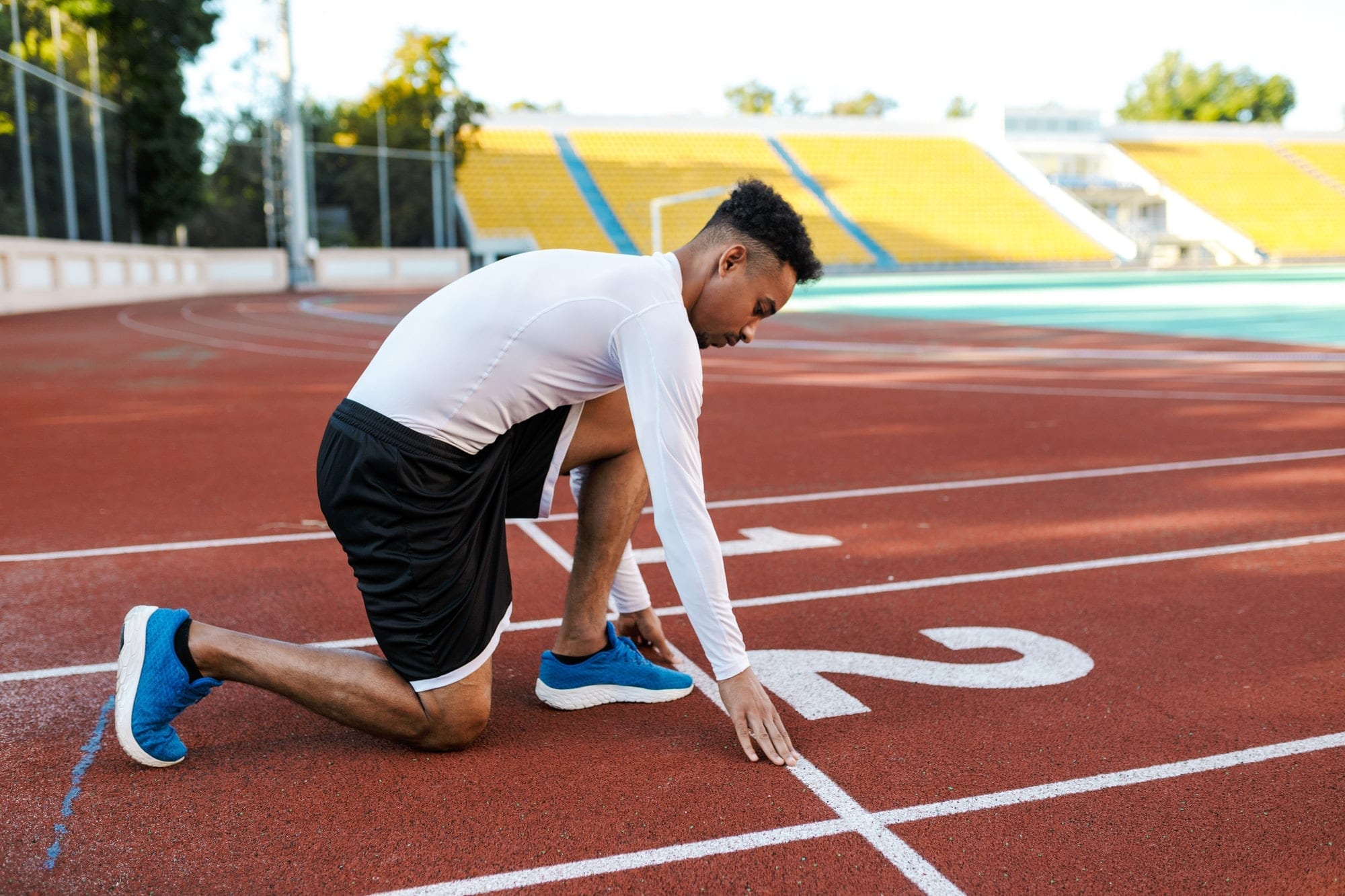 Young attractive African American sportsman preparing for running on racetrack at city stadium