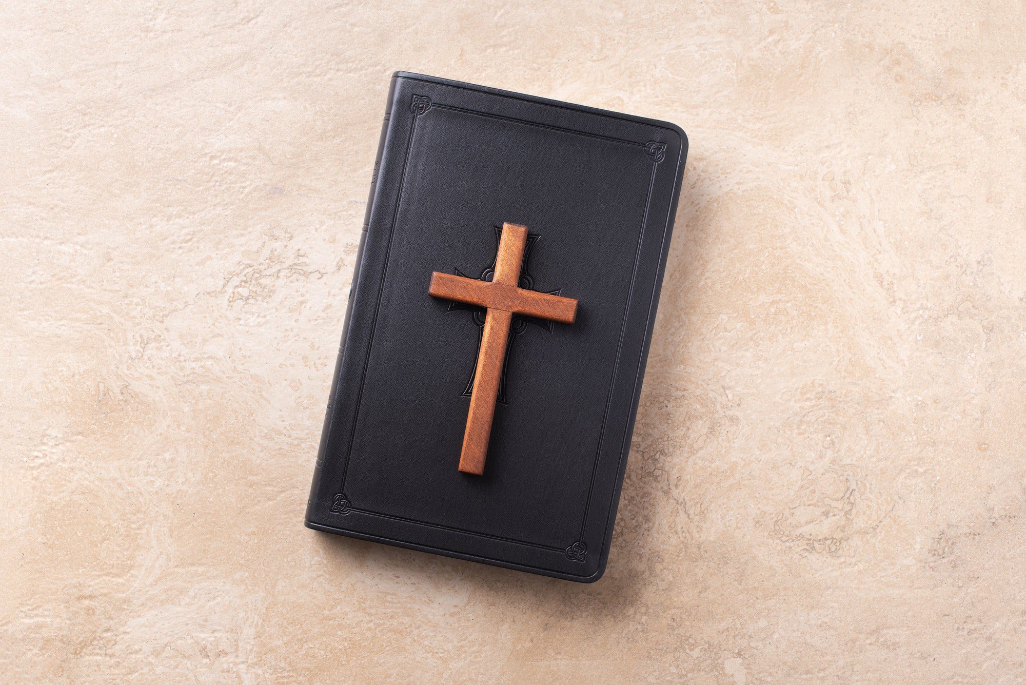 Wooden cross on Bible over marble background. Reminder of Jesus sacrifice and Christ resurrection