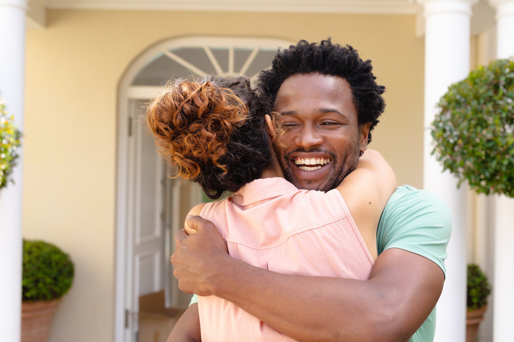 Cheerful young african american man hugging girlfriend against house
