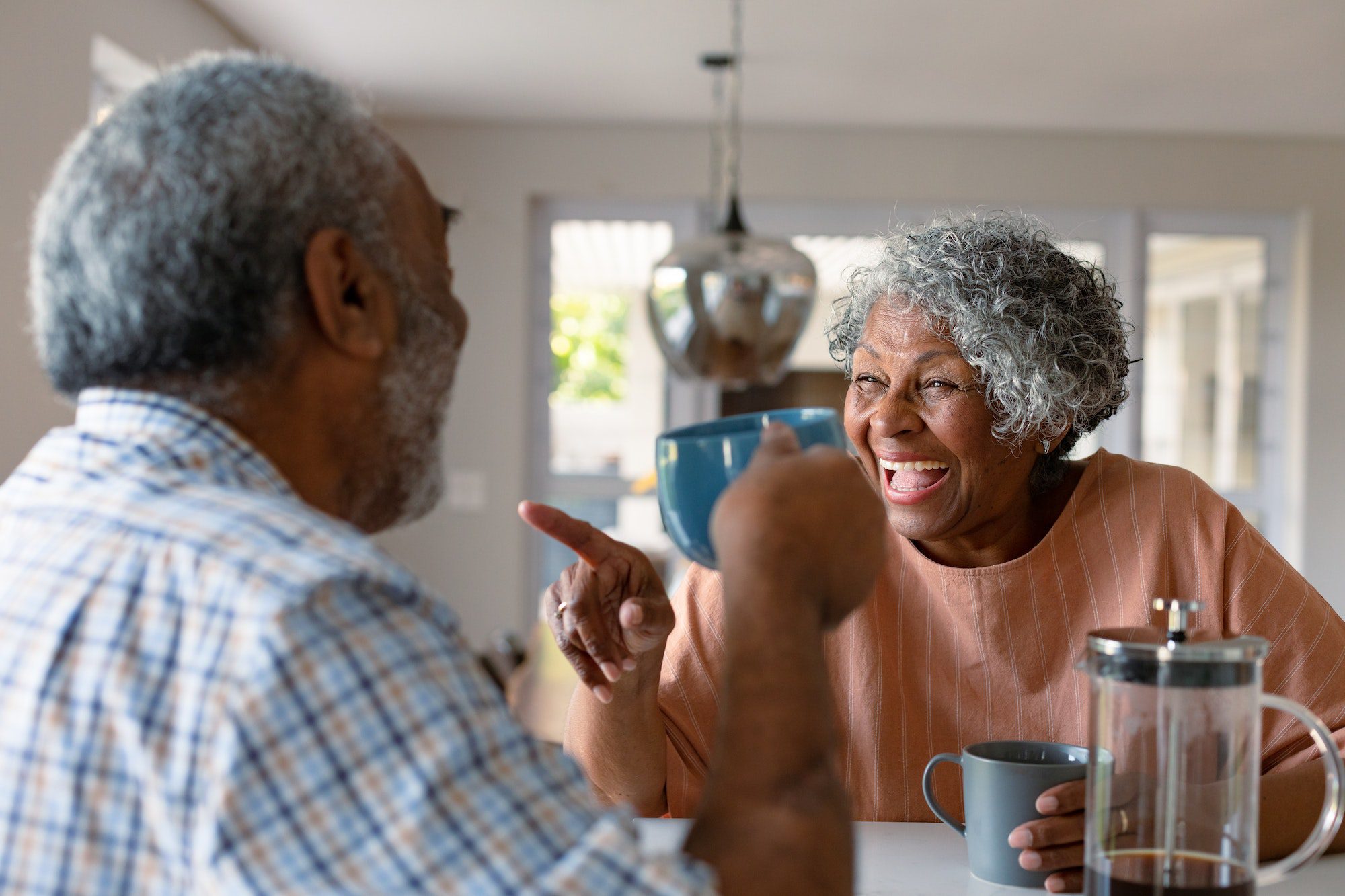 Happy african american senior couple sitting in kitchen with coffee and talking