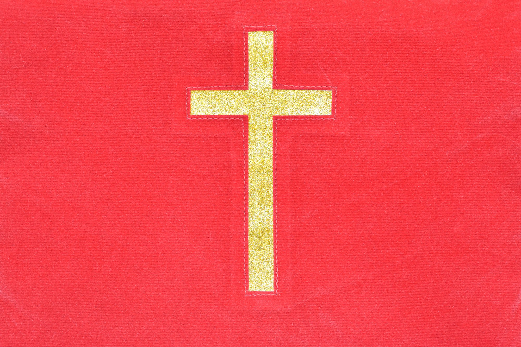 Gold catholic cross on red cloth texture